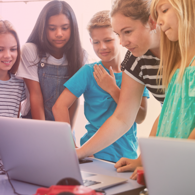 Children surrounding teacher showing something on a laptop